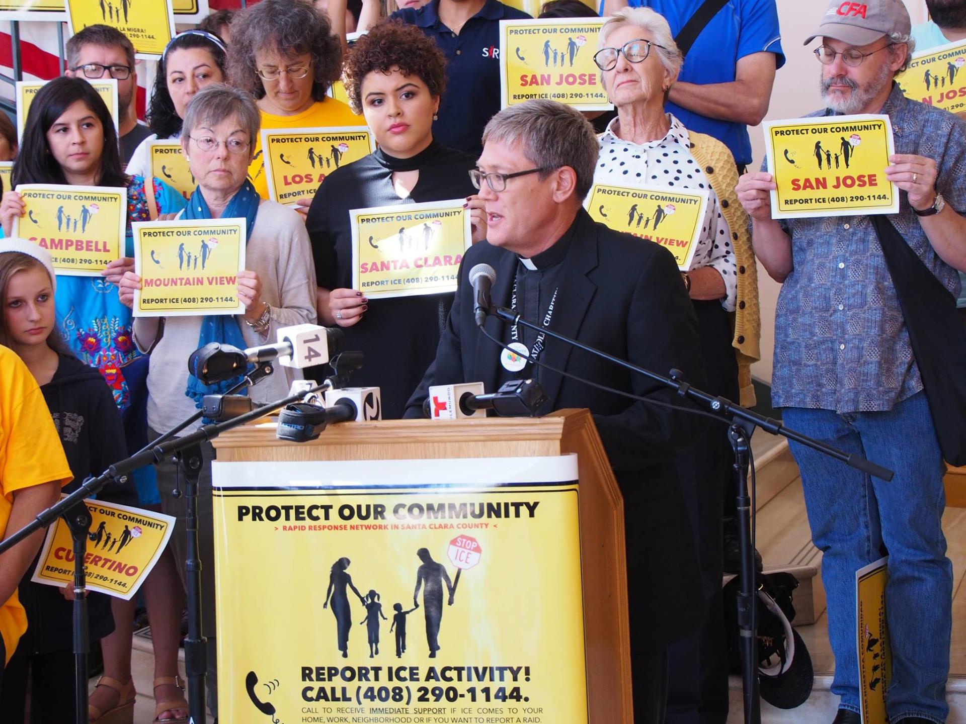 Person giving speech at podium with sign that reads Protect Our Community